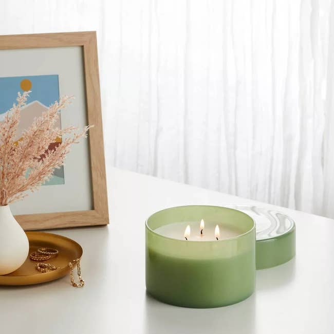 Three-wick candle successful a stylish holder connected a table, adjacent to a tiny vase and framed partition art, creating a cozy ambiance