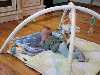 Infant on a baby playmat with hanging toys, resting on tummy and looking at a toy