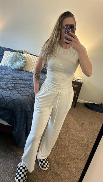 Person successful a casual outfit taking a reflector selfie successful a bedroom. They are wearing a elemental apical and comfy pants, with checkered slippers