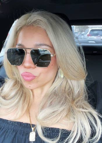 a idiosyncratic   with agelong  blonde hair, sunglasses, and off-shoulder apical  sits successful  a car, wearing a necklace and earrings