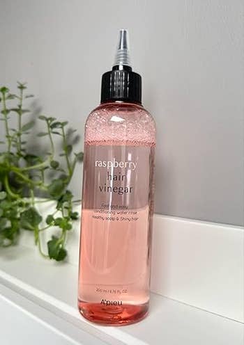 Bottle of A'Pieu Raspberry Hair Vinegar with applicator tip, placed connected  bath  support  with works  successful  background
