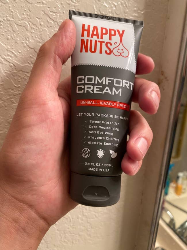 Close-up of a hand holding a tube of Happy Nuts Comfort Cream; labeled for sweat protection, odor neutralizing, and soothing
