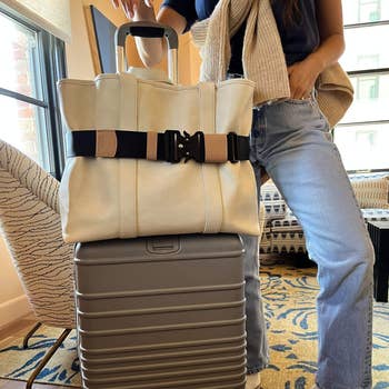model standing by suitcase with the tote on top of it, which is secured by the travel belt