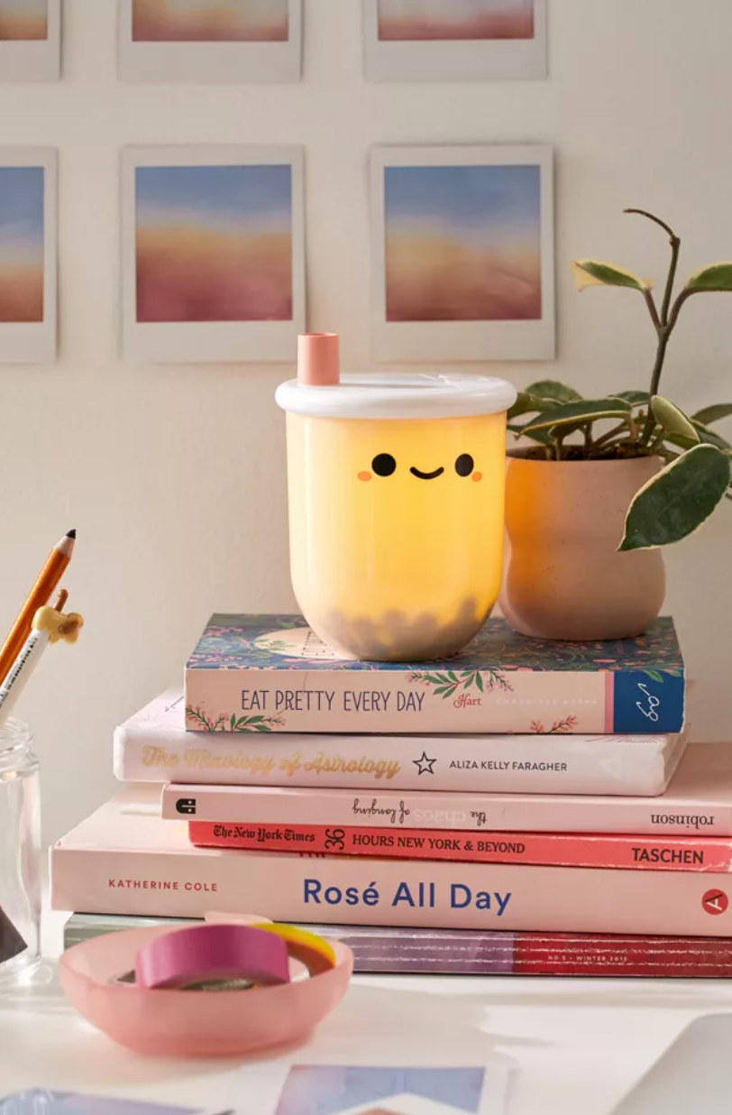 Cute smiling boba-tea-shaped desk lamp on top of big stack of books
