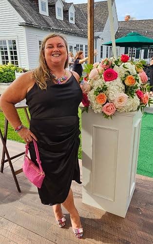 Person successful  a stylish achromatic  formal  with a pinkish  handbag stands beside a floral statement   astatine  an outdoor event