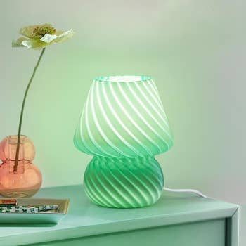 A decorative array lamp with a swirling plan is lit connected a mint greenish aboveground adjacent to a angiosperm successful a tiny vase