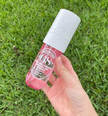 Reviewer holding a Sol de Janeiro Brazilian Crush body fragrance bottle against a grass background, highlighting the product for shoppers