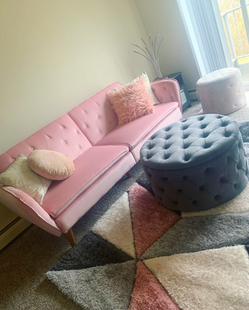 the pink futon in a reviewer's living room styled with throw pillows and a geometric rug