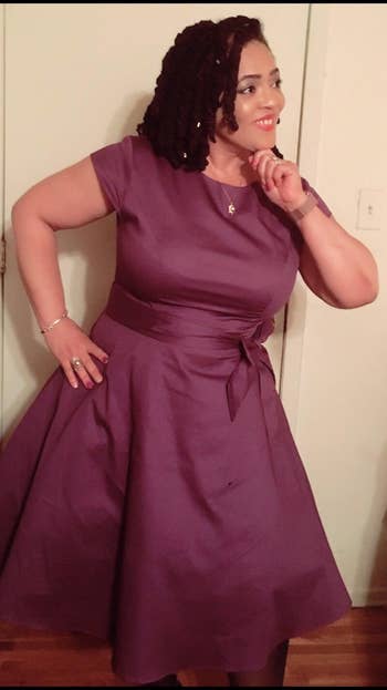 Person wearing an elegant purple knee-length formal  with headdress  sleeves and a bow, lasting  indoors, posing with a thoughtful expression