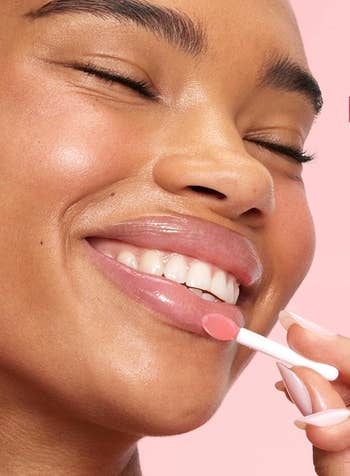 Person smiling portion applying articulator gloss with an applicator, illustrating quality merchandise usage