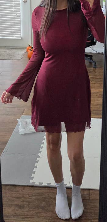 Person wearing a sheer long-sleeved, knee-length dress, taking a reflector  selfie. The mounting  suggests casual location  attire