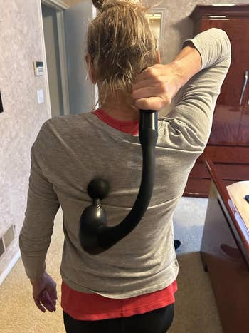 Person using a black massage tool on their back in a home setting