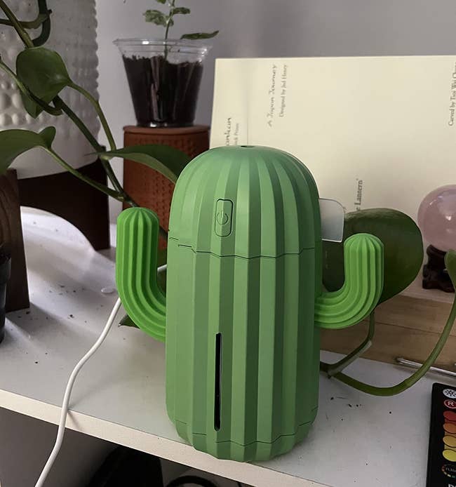 reviewer's green humidifier with two arms that looks like a cactus with steam coming out of it