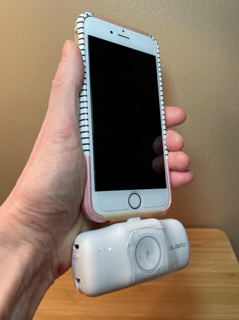 Hand holding a smartphone attached to a white charging device 