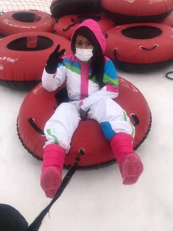 Person successful  a snowsuit and disguise  sitting successful  a reddish  snowfall  tube, posing with a bid    sign, acceptable   connected  a snowy outdoor surface