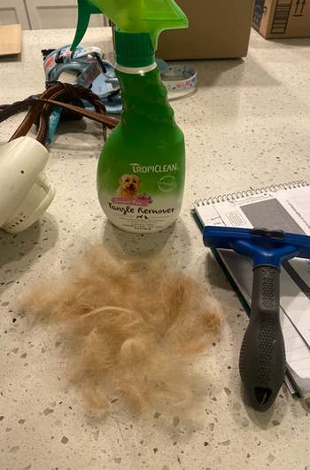 the green bottle of detangling shampoo next to a pile of loose fur and a grooming tool