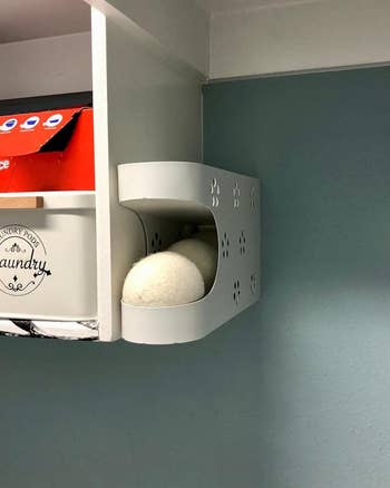 A wall-mounted laundry dispenser with wool dryer balls and a box of fabric softener sheets on a shelf above