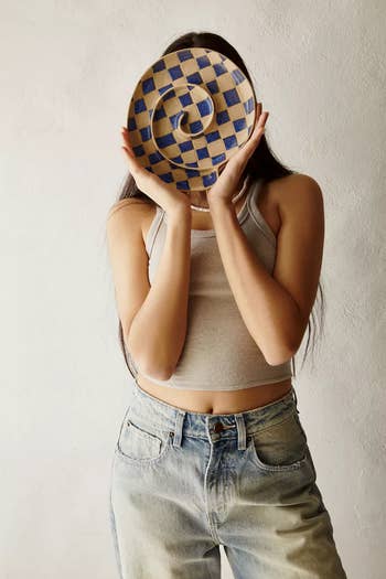 Model holding a blue and cream checkered serving plate with grooves in a swirling patter 