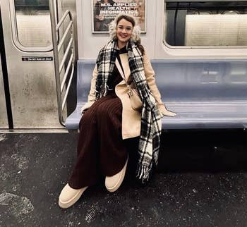 Person successful a stylish overgarment and scarf seated connected a subway bench, with buying ads disposable successful the background