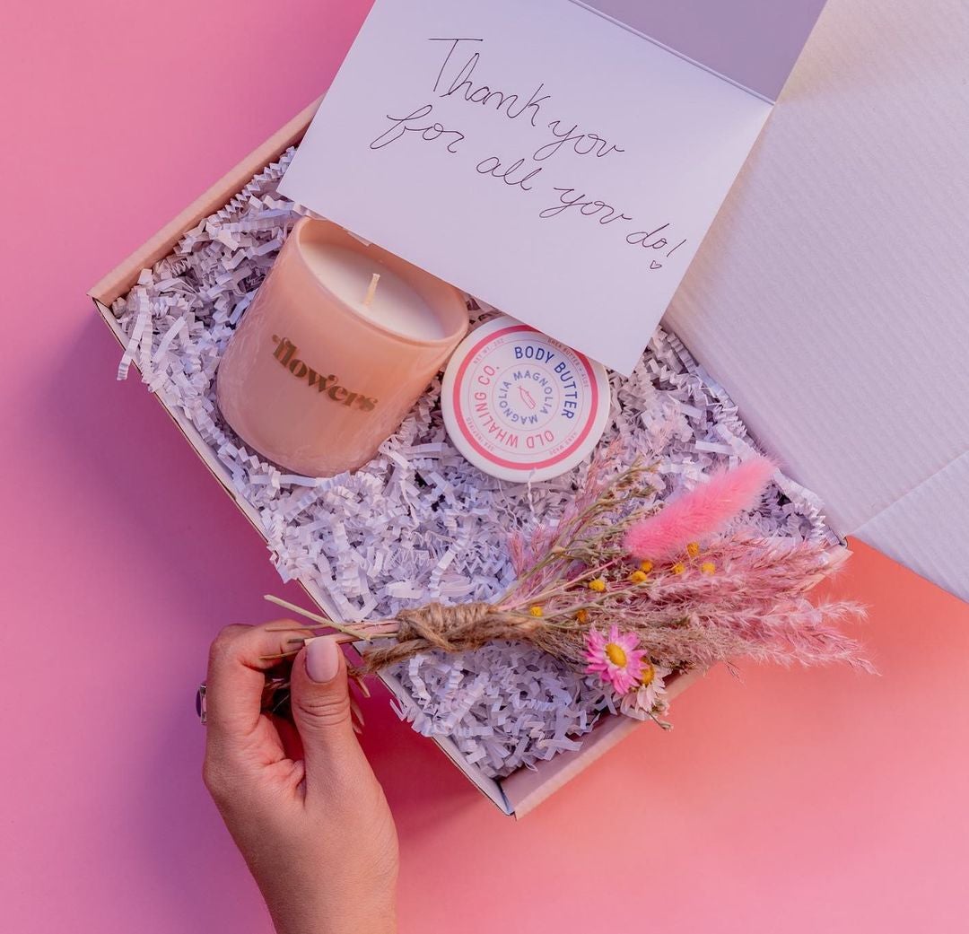 photo of a gift box filled with a candle, body butter, fake flowers, and a card that reads thank you for all you do
