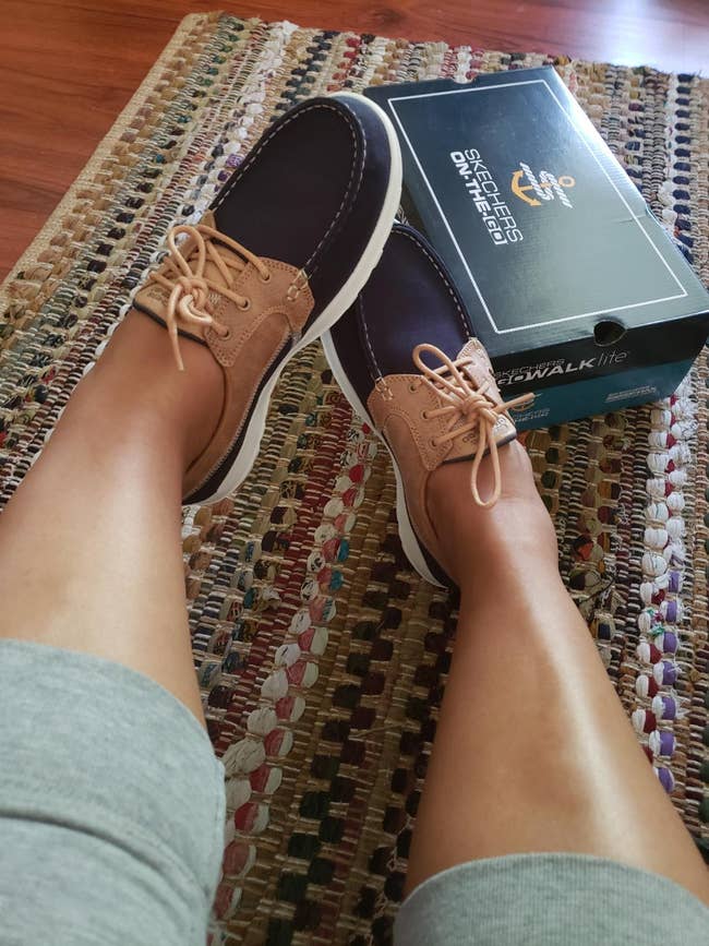 Person wearing vessel shoes with relaxed acceptable design, seated connected a colorful rug, adjacent to a Skechers shoebox