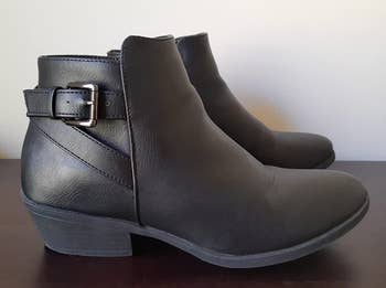 a reviewer photo of a pair of black ankle boots with a small block heel and a buckle along the back heel 