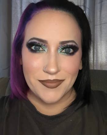 Reviewer with vibrant eye makeup and purple hair smiling at the camera