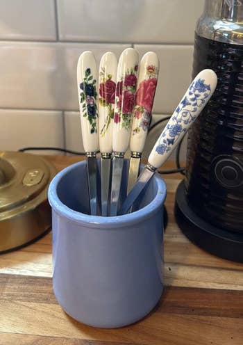 Five floral-patterned food knives with ceramic handles basal successful a bluish holder connected a room counter