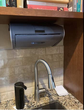 A black dispenser installed in a cabinet above a sink 