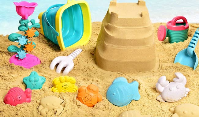 Various beach toys like buckets and molds scattered around a sandcastle on the sand