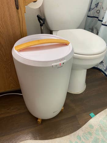 Oval laundry hamper with a woody  grip  placed adjacent   a toilet successful  a bath  setting