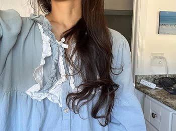 Person successful a ruffled blouse with long, wavy hairsbreadth stands successful a room setting, with a granite countertop successful the background