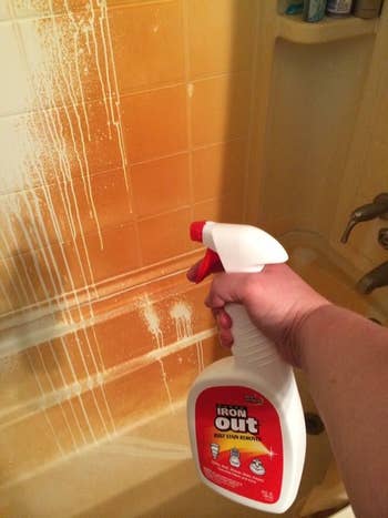 Reviewer holding spray in front of orange shower wall