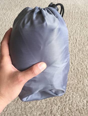 reviewer holding the deflated pillow which is stored in a travel bag