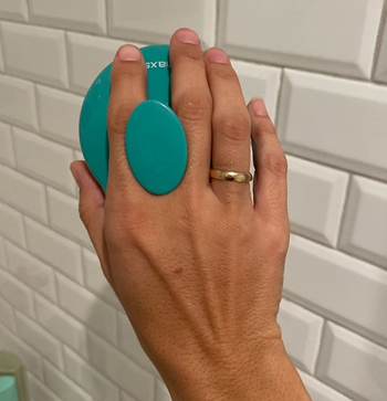 reviewer holding the handle of the green scalp massager between their fingers