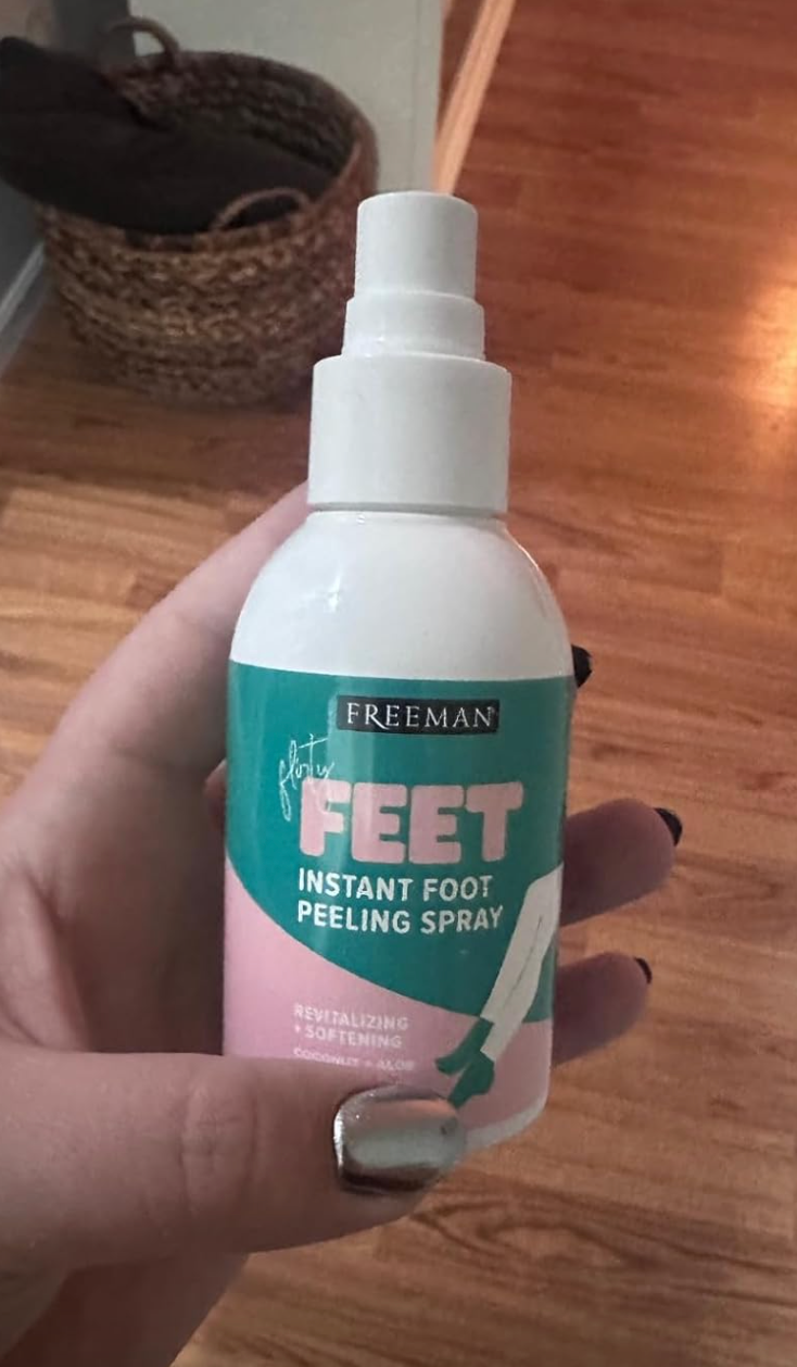 A hand holds a bottle of Freeman instant foot peeling spray for revitalizing and softening feet