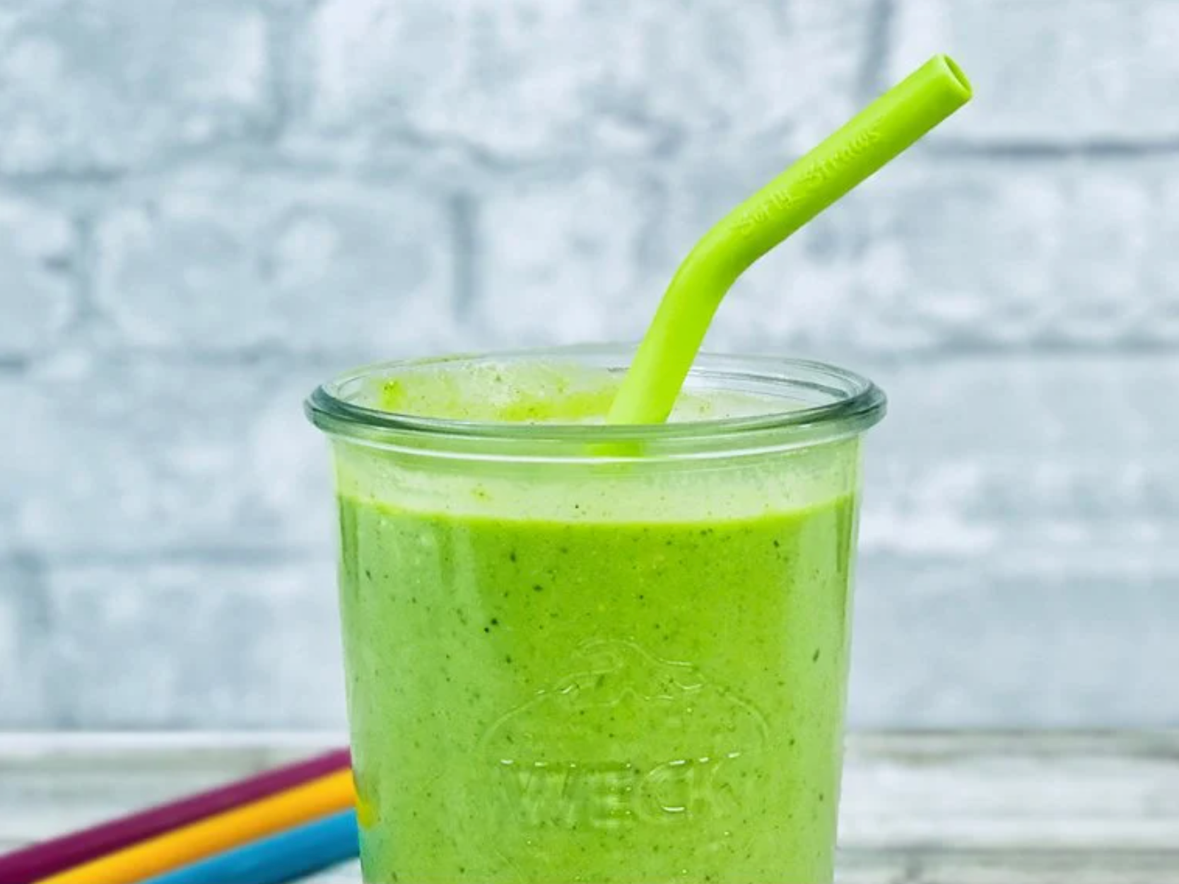 a green silicone straw in a glass cup full of a green smoothie