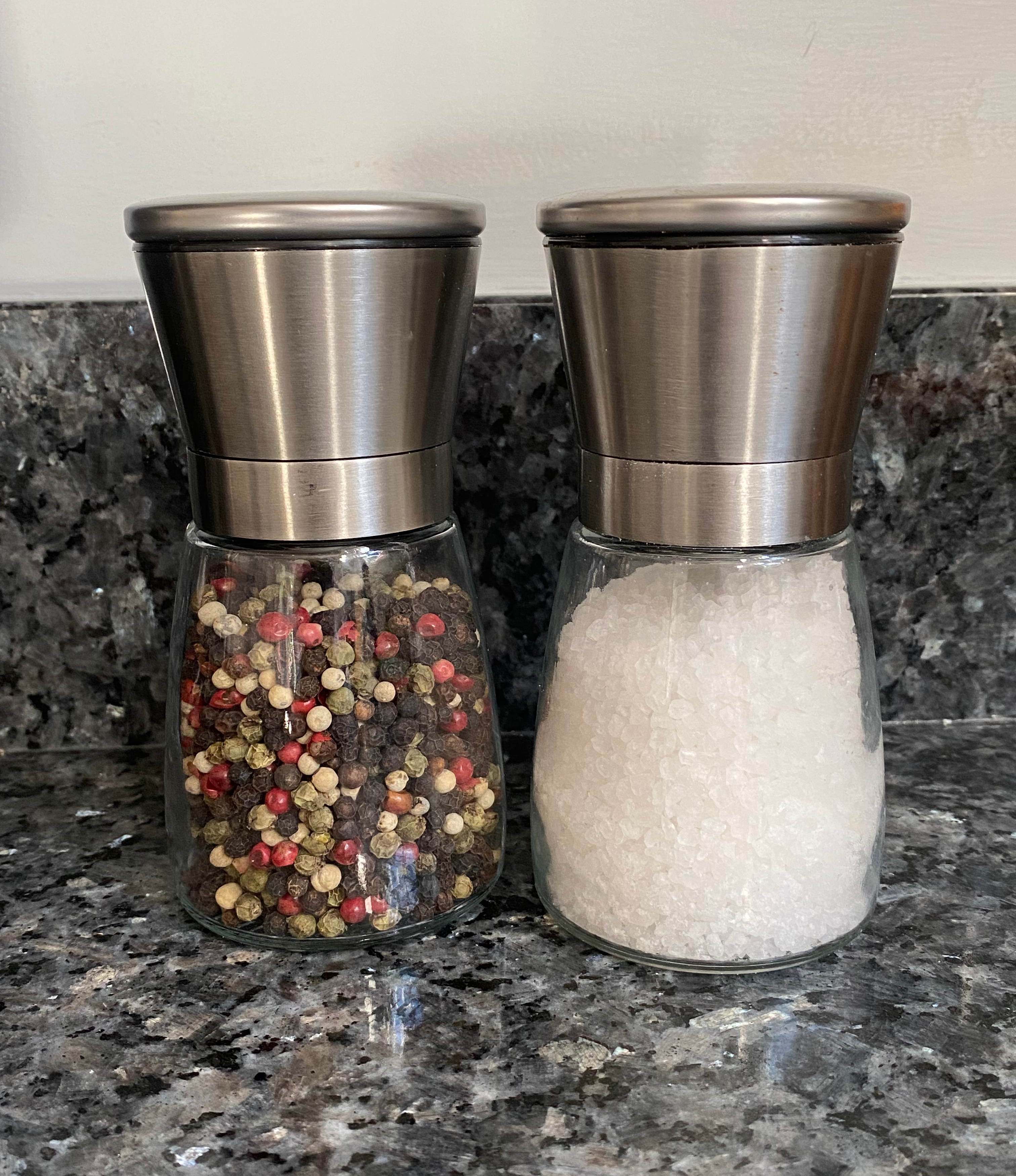 Two glass grinders with stainless steel tops full of pepper and sea salt