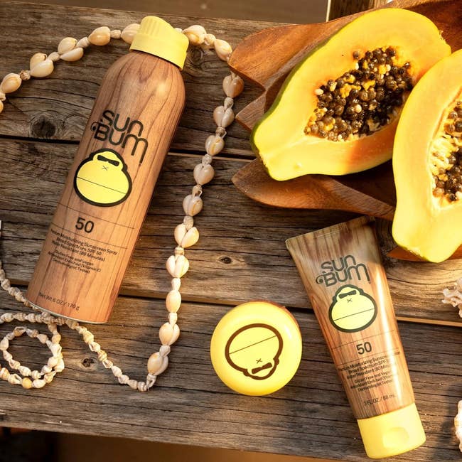 Sun Bum sunscreen products with SPF 50 are displayed adjacent to halved papaya and a ammunition necklace connected a woody table