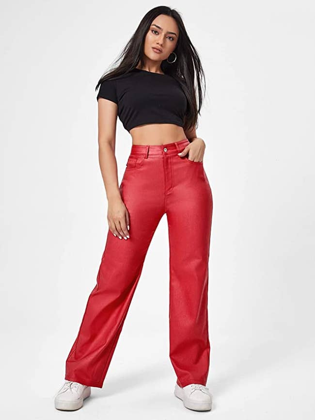 Model wearing bright red straight fit faux leather pants with white sneaker and a black short sleeve crop top