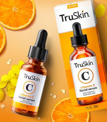 TruSkin Vitamin C serum bottle beside its packaging, with citrus slices and flowers around it