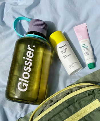 bottle of Invisible shield next to a tube of balm dot com and a glossier water bottle