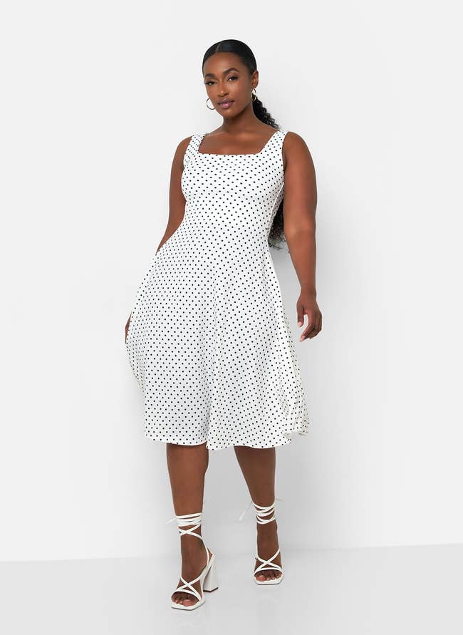 Model in a white polka-dot dress and white strappy heels poses