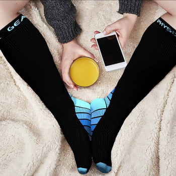 Model wearing the blue-and-black compression socks while on their phone and holding a glass of juice