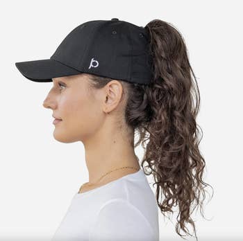 Side profile of a person wearing a baseball cap with a curly ponytail sticking out