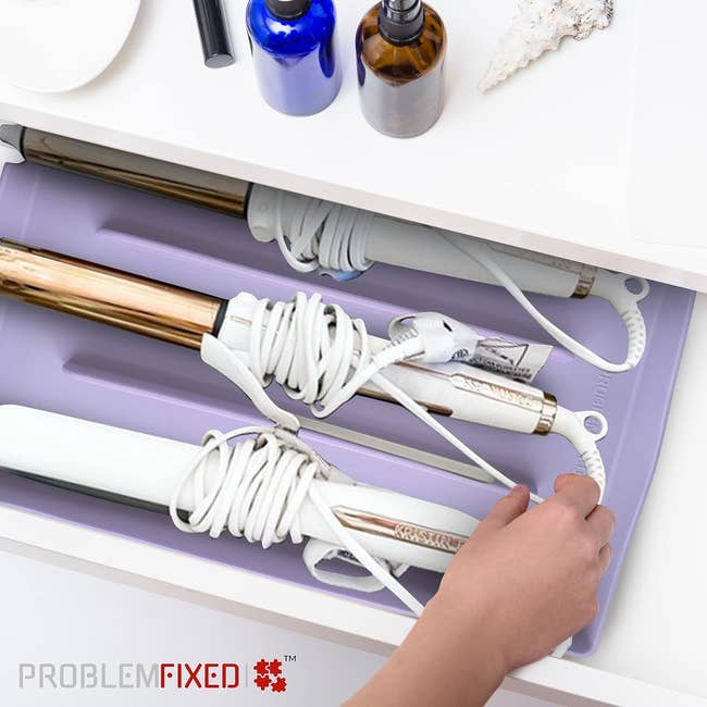 A idiosyncratic organizes styling tools successful a drawer utilizing a silicone mat designed to support cords from tangling. The representation is from the marque Problem Fixed® and features neatly arranged styling devices