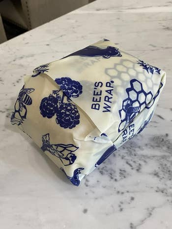 Bee's Wrap with bee and honeycomb designs, wrapped around a package on a marble surface