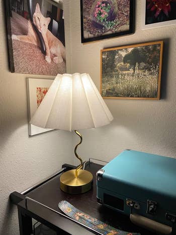 A stylish lamp with a pleated shadiness  connected  a array  adjacent  to a teal suitcase and decorative partition  art