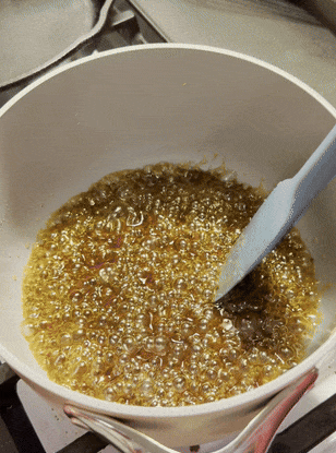 Cooking caramel sauce in a pot with a spatula stirring bubbling mixture, highlighting homemade cooking essentials