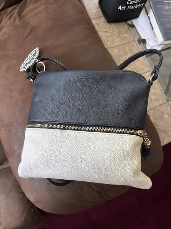 Two-tone handbag with a zippered upper compartment and an adjustable strap, resting on a brown surface